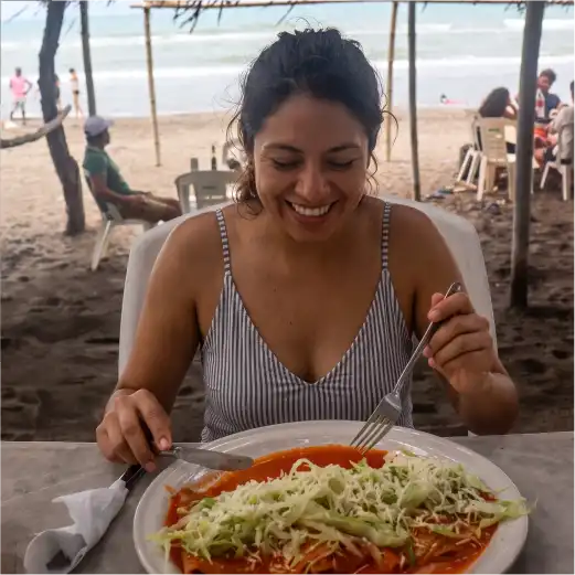 Mujer sonriente disfrutando de un desayuno tradicional frente al mar en el restaurante Palapa Mar Azul, Playa de Monte Gordo