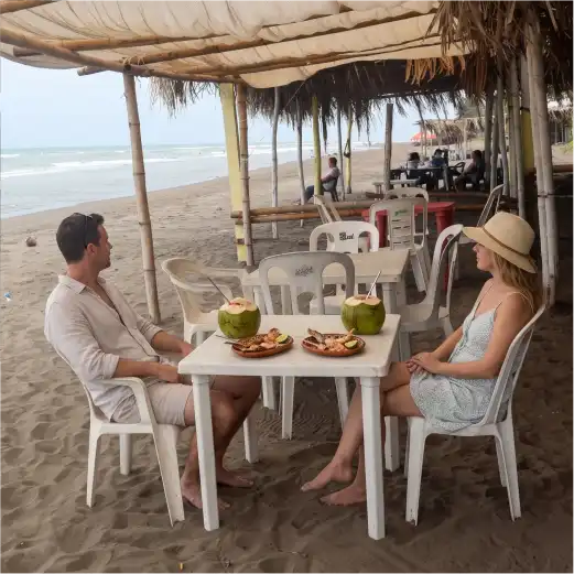 Pareja disfrutando de mariscos frescos y cocos bajo una palapa frente al mar en el restaurante Palapa Mar Azul, Playa de Monte Gordo
