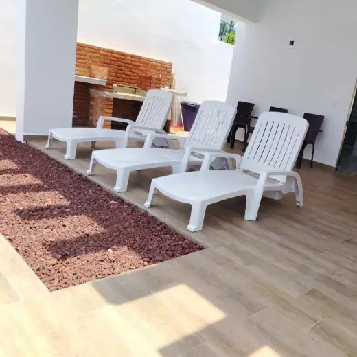 Terraza techada en Villa Tortuga con tres camastros blancos para asolearse y un amplio asador de ladrillo rojo al fondo para reuniones.