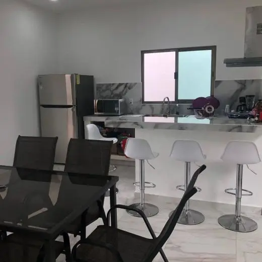 Comedor y cocina de concepto abierto en Villa Tortuga, Costa Esmeralda, con mesa de comedor de vidrio negro y sillas negras a juego, barra desayunadora con cuatro taburetes blancos y cocina moderna totalmente equipada con electrodomésticos de acero inoxidable y ventana de vidrio esmerilado.